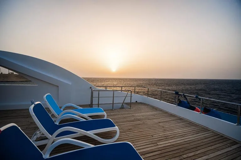 Terrasse d'un bateau de plongée avec transats face au soleil couchant