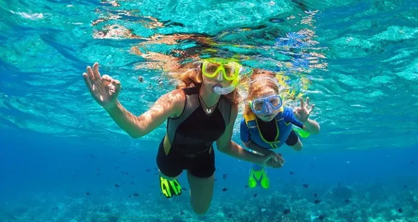 Deux personnes sourient et font des signes sous l'eau