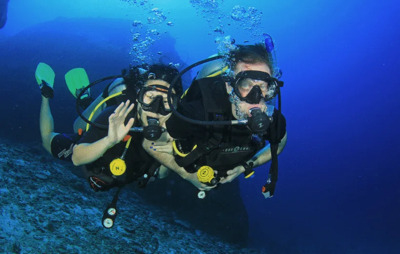 Deux plongeurs souriants nagent ensemble dans une eau bleue claire