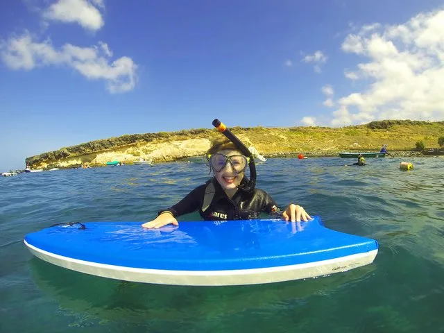 Plongeuse souriante sur planche bleue en mer, paysage côtier en arrière-plan