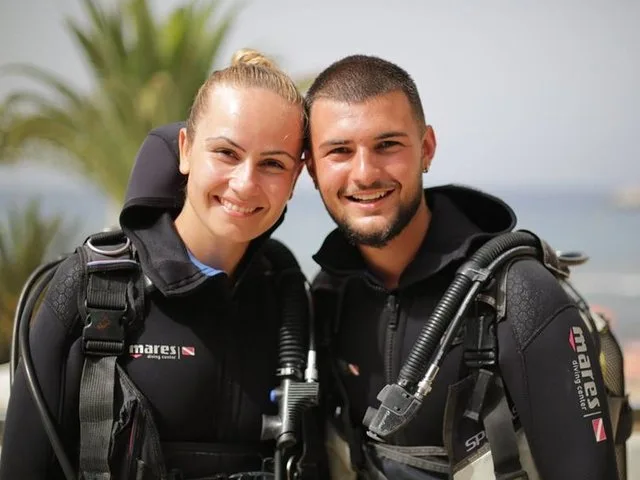 Deux plongeurs souriants en combinaison, équipés et prêts à plonger