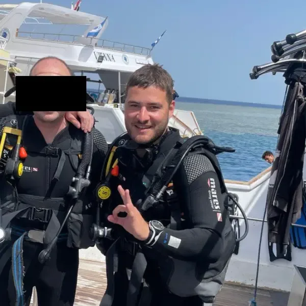 Deux plongeurs souriants sur un bateau, équipés et prêts à plonger