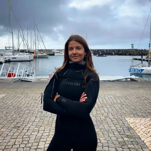 Femme en combinaison de plongée souriante devant des bateaux amarrés