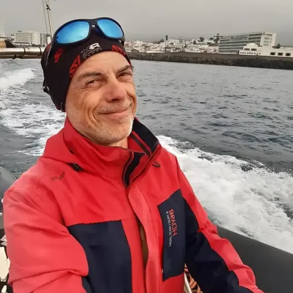 Homme souriant portant une veste rouge et des lunettes de soleil en mer