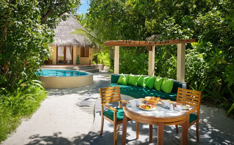Petite piscine, salon extérieur et bungalow avec végétation luxuriante