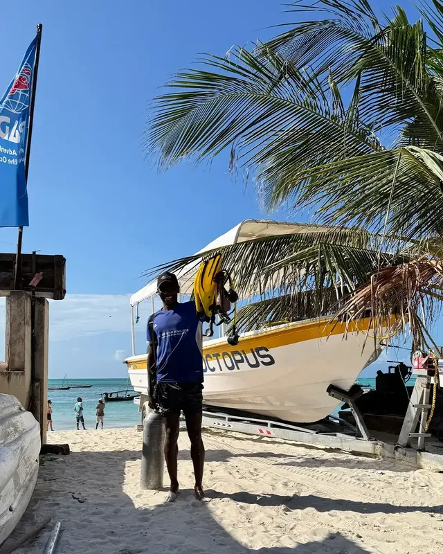 Plongeur tenant son équipement devant un bateau jaune sur plage