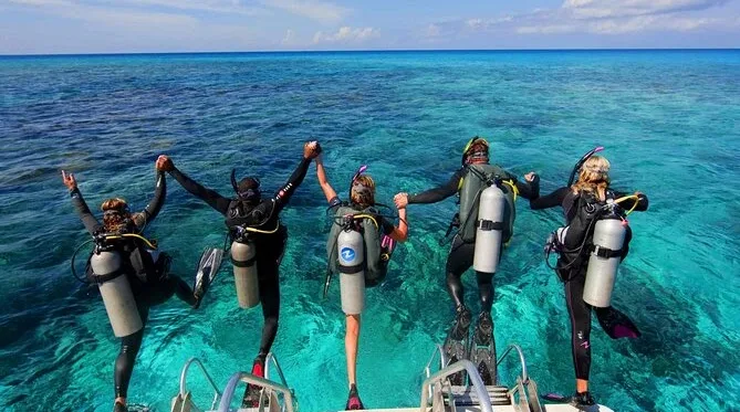 Plongeurs équipés sur un bateau, bras levés, mer turquoise ensoleillée