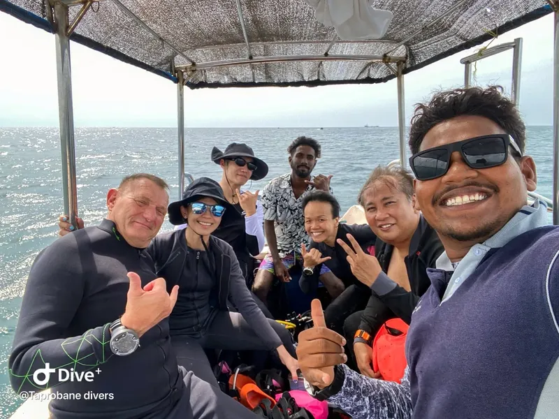 Groupe de plongeurs souriants sur un bateau en mer, signe de la main