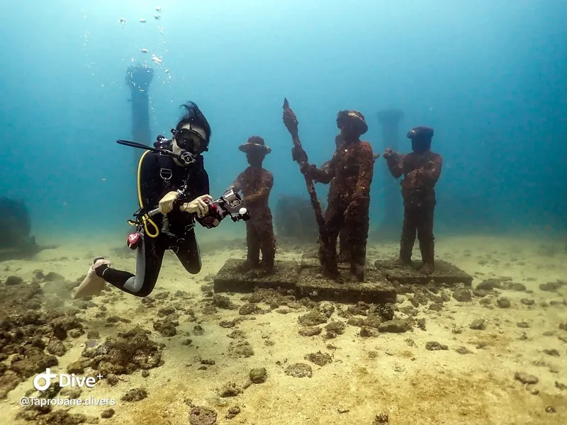 Plongeuse explorant une sculpture sous-marine avec des personnages anciens