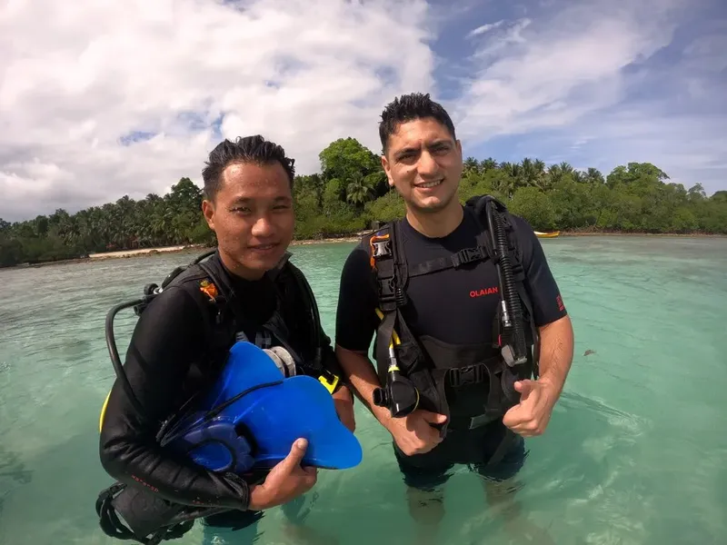 Deux plongeurs souriants en combinaison dans une eau turquoise peu profonde