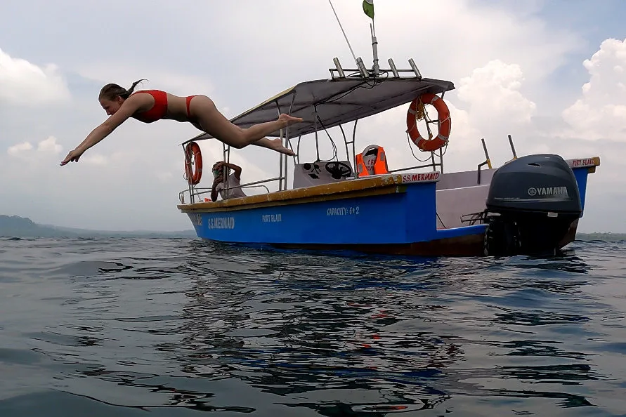 Une plongeuse saute d'un bateau bleu en mer, plusieurs personnes à bord