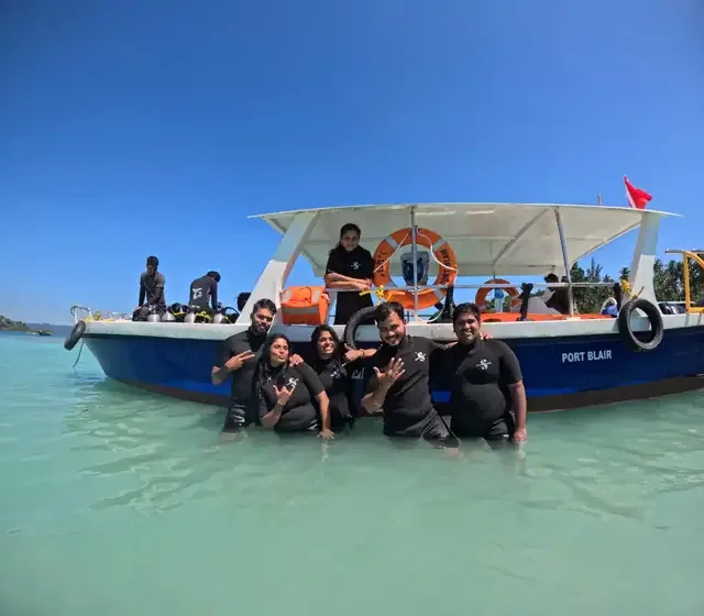Groupe de plongeurs souriants devant un bateau bleu en mer turquoise