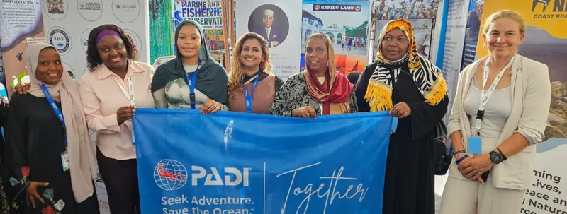 Groupe de personnes souriantes tenant une bannière PADI bleue et blanche
