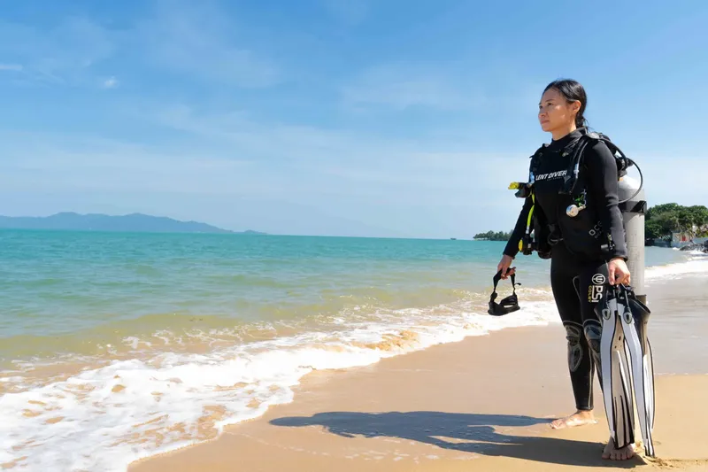 Plongeuse en combinaison sur une plage de sable avec son équipement