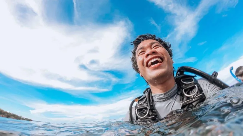 Plongeur souriant, équipé, émergeant de l'eau sous un ciel bleu clair