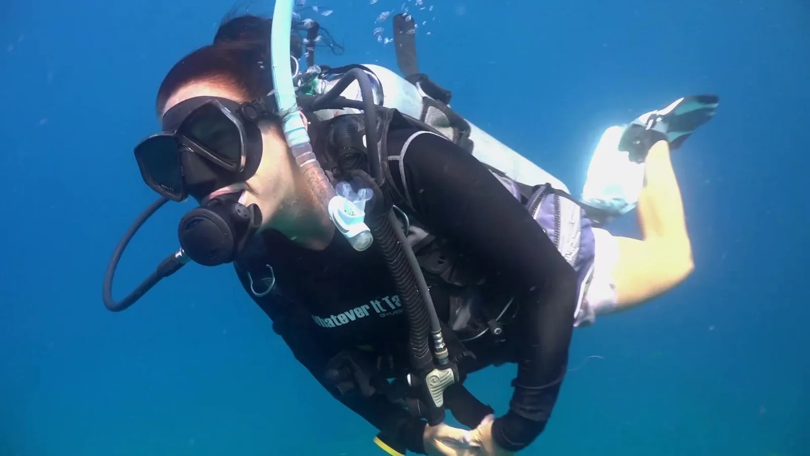 Plongeuse en combinaison noire nageant dans une eau bleue claire