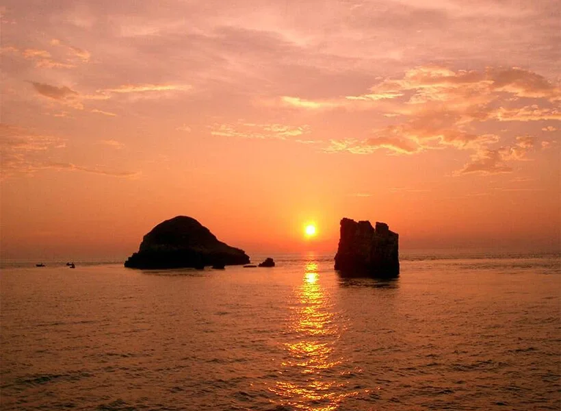 Coucher de soleil sur l'océan avec des rochers et un bateau