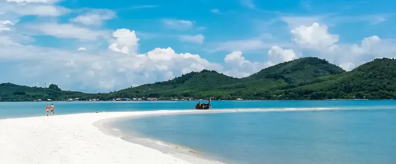 Plage de sable blanc, deux personnes et un bateau au loin