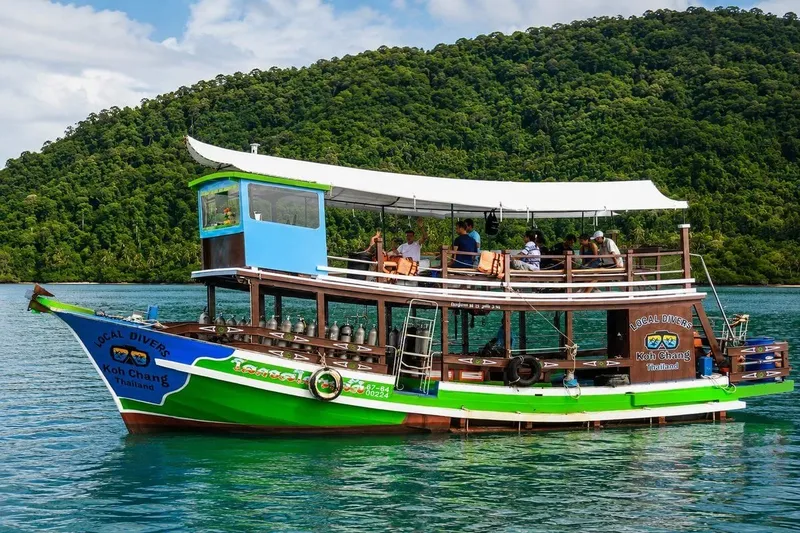 Bateau de plongée longtail vert et bleu amarré dans une baie tropicale