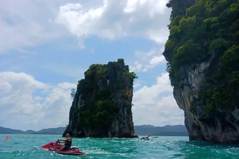Jet ski navigue devant une formation rocheuse et une falaise verte
