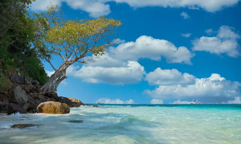 Plage tropicale avec eau turquoise, ciel bleu et quelques bateaux