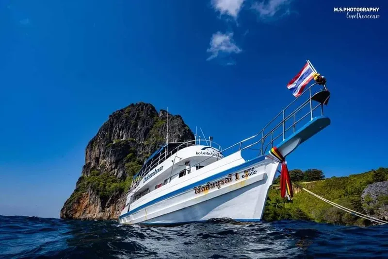 Bateau de plongée amarré près d'une île rocheuse sous ciel bleu