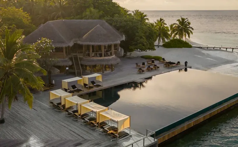 Bâtiment avec toit de chaume, piscine, plage et végétation tropicale