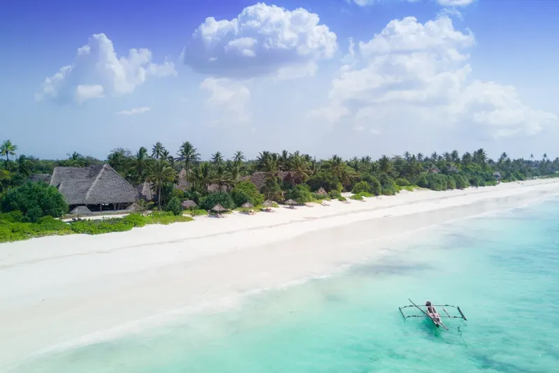 Plage de sable blanc, eau turquoise, quelques bungalows et un petit bateau