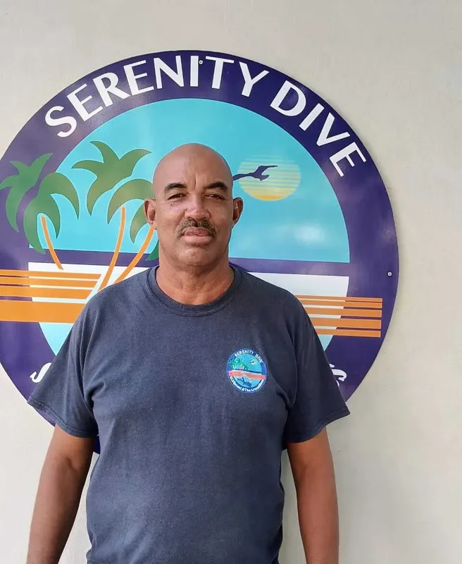Homme souriant devant un décor tropical avec l'inscription Serenity Dive
