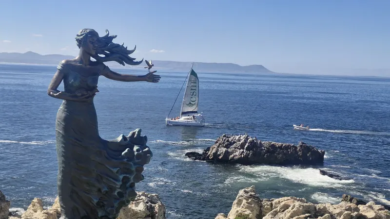 Statue de femme face à la mer, voilier et côte rocheuse