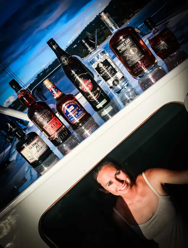 Femme souriante sur un bateau avec des bouteilles d'alcool alignées