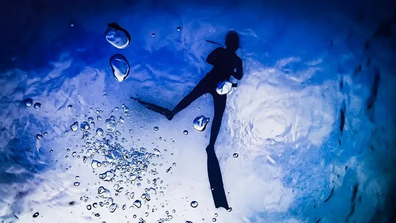 Plongeur en combinaison noire nageant vers le haut dans l'eau bleue