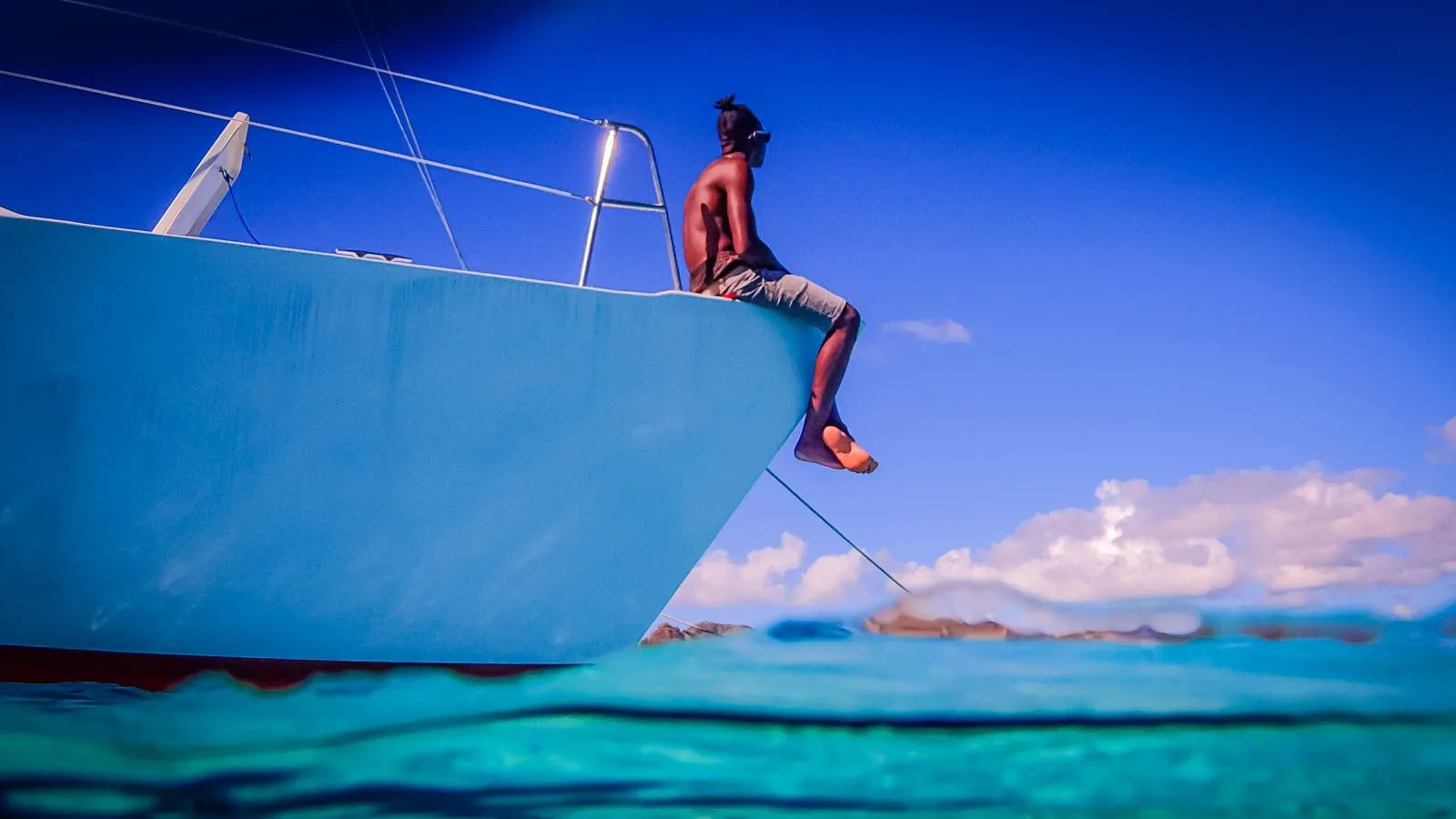 Homme assis sur la coque d'un bateau, vue sous-marine, ciel bleu