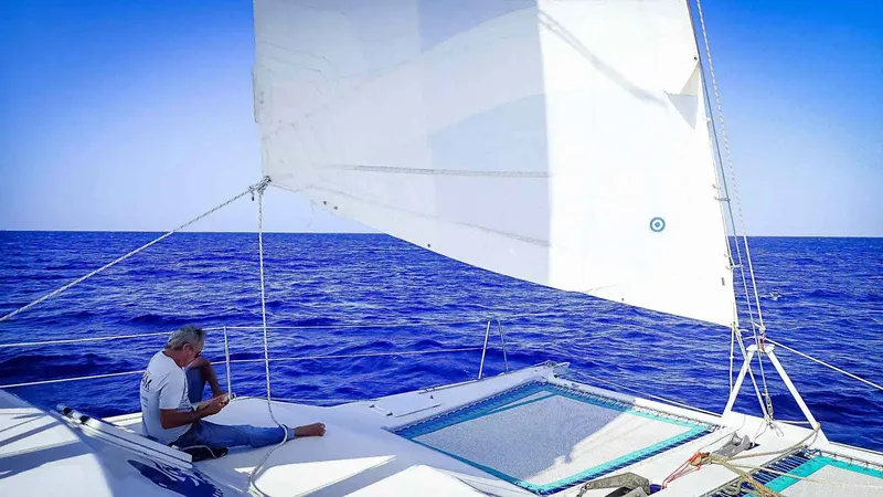 Homme assis sur la proue d'un catamaran en pleine mer