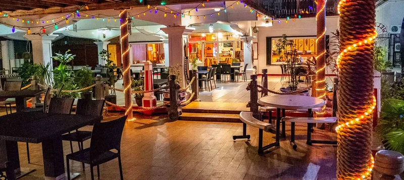 Terrasse éclairée avec tables, chaises et végétation tropicale lumineuse
