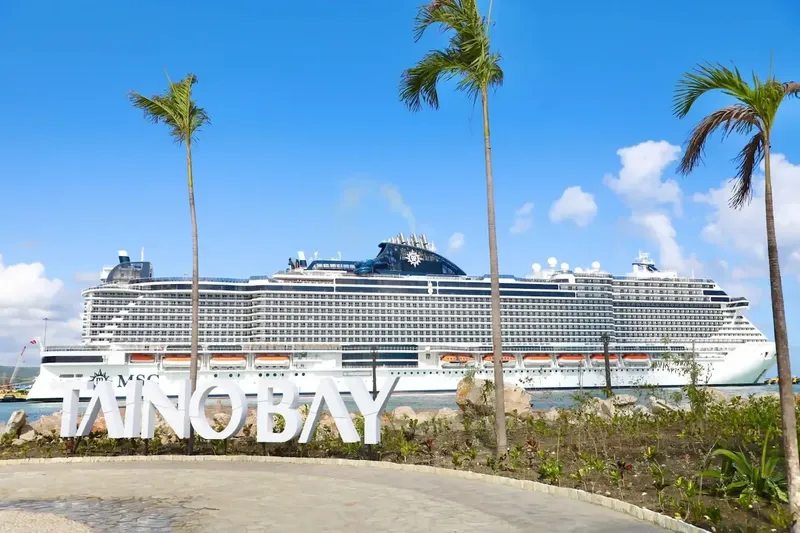 Grand paquebot de croisière amarré devant des palmiers et un lettrage