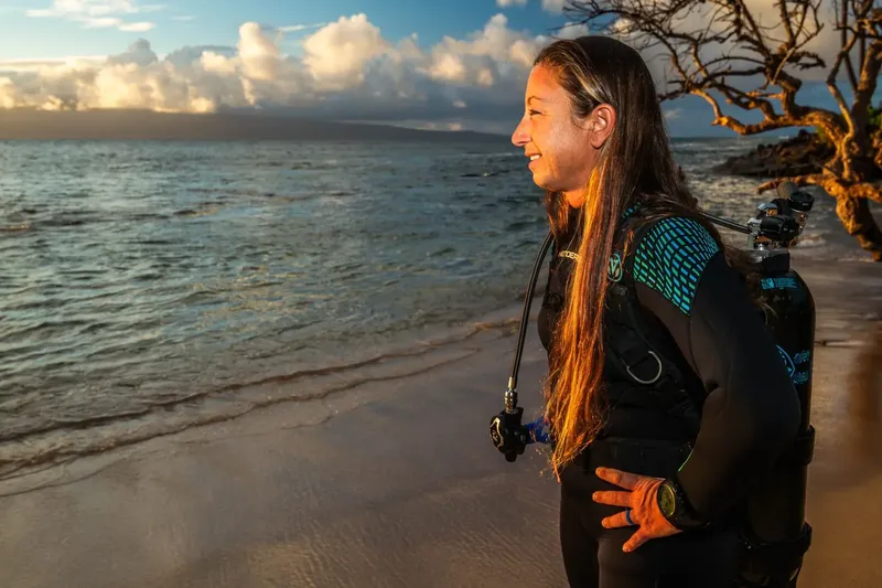 Plongeuse souriante sur une plage, équipement de plongée sur le dos