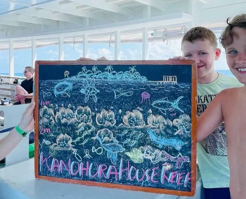 Deux enfants souriants présentent un tableau illustrant un récif corallien