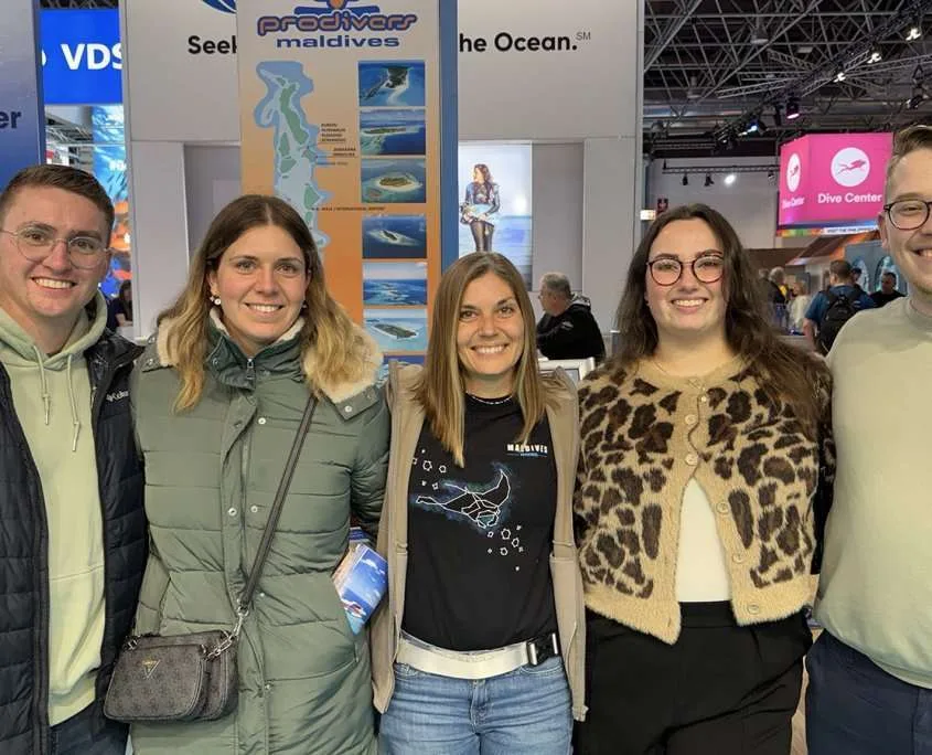 Groupe de cinq personnes souriantes posant devant des stands de salon