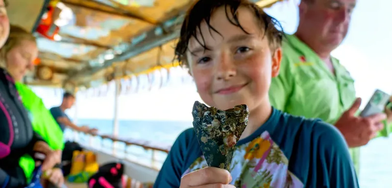 Enfant souriant sur un bateau, tenant un objet trouvé en mer