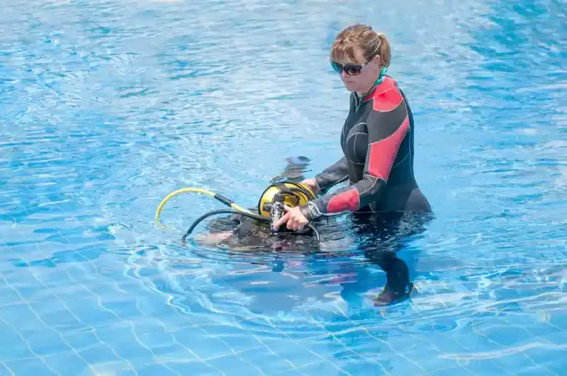 Une plongeuse en combinaison prépare son équipement dans une piscine