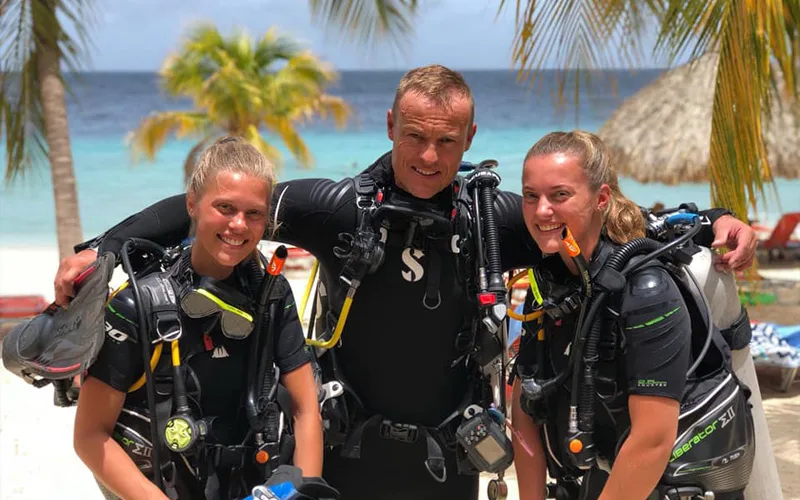 Trois plongeurs souriants équipés sur une plage tropicale ensoleillée