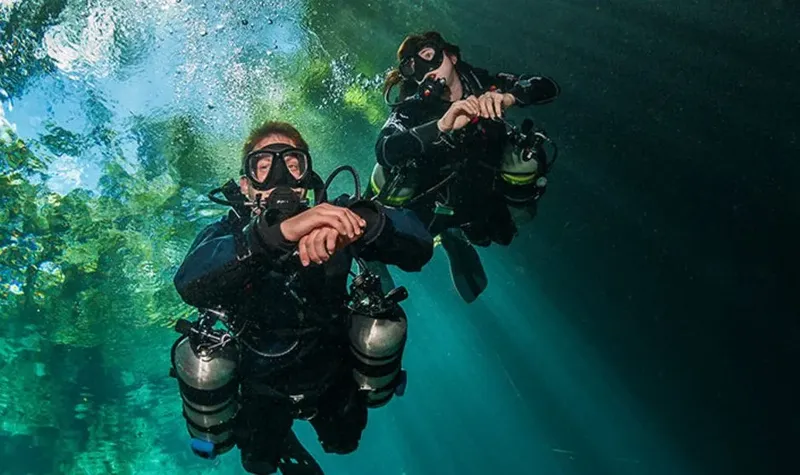 Deux plongeurs souriants en combinaison, équipés, flottent dans l'eau