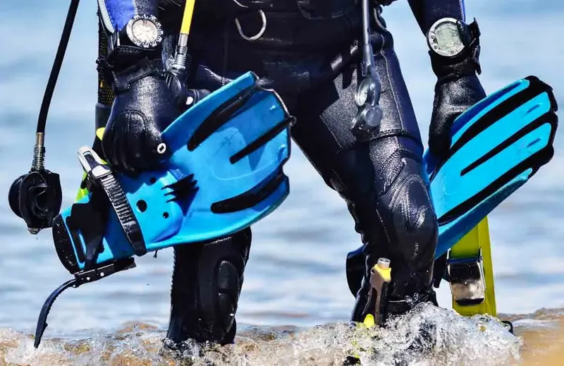 Plongeur en combinaison sortant de l'eau avec palmes bleues