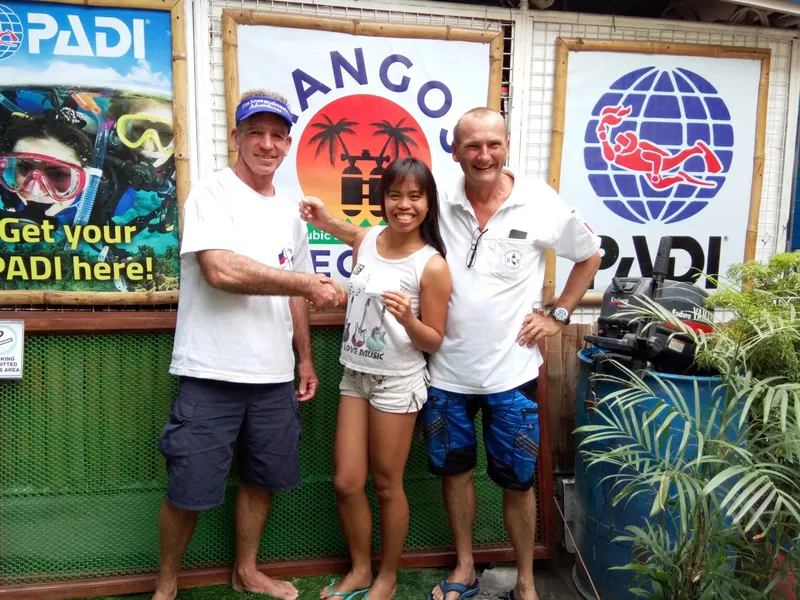 Trois personnes souriantes posent devant des affiches de plongée PADI