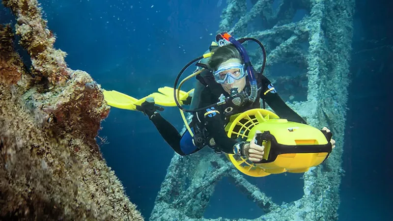 Plongeuse utilisant un scooter sous-marin près d'une structure métallique