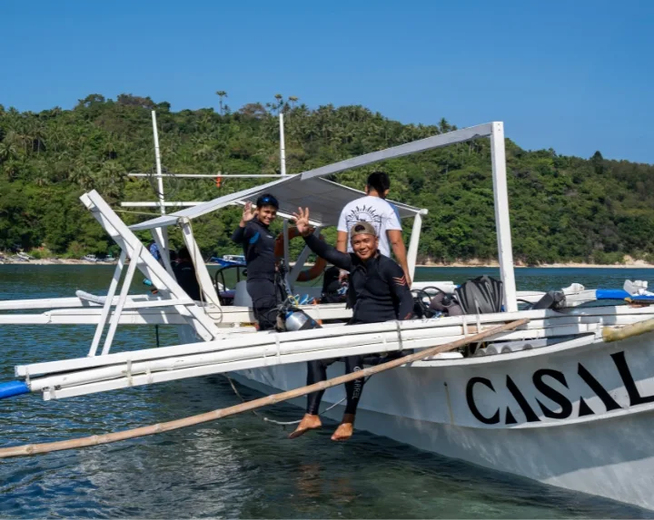 Trois plongeurs souriants sur un bateau blanc, paysage insulaire en arrière-plan