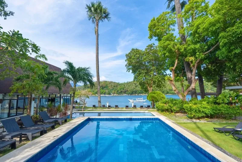 Piscine bleue devant un bâtiment tropical et des bateaux amarrés