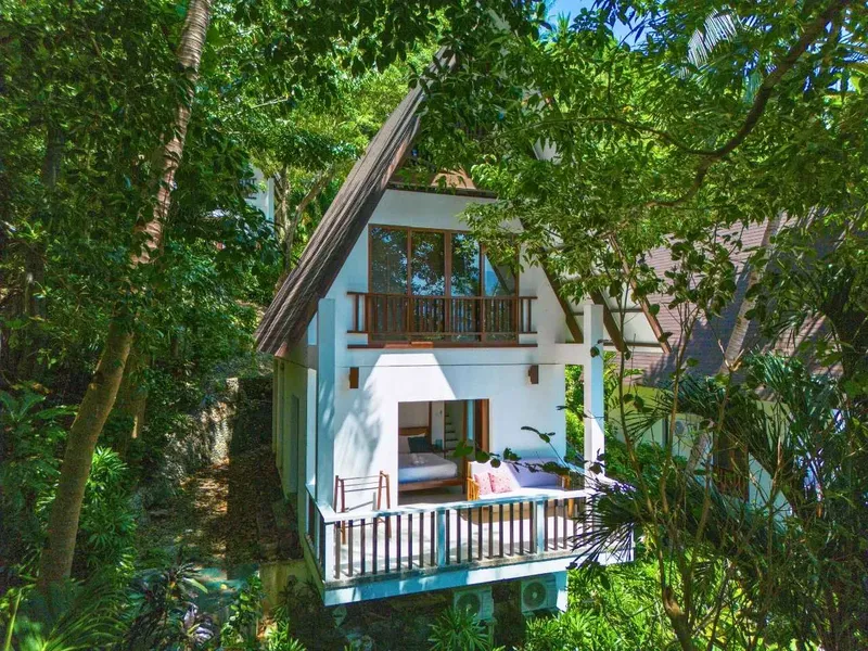 Petite maison blanche avec balcon entourée d'une végétation luxuriante