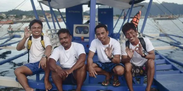 Quatre hommes souriants assis sur un bateau de pêche traditionnel
